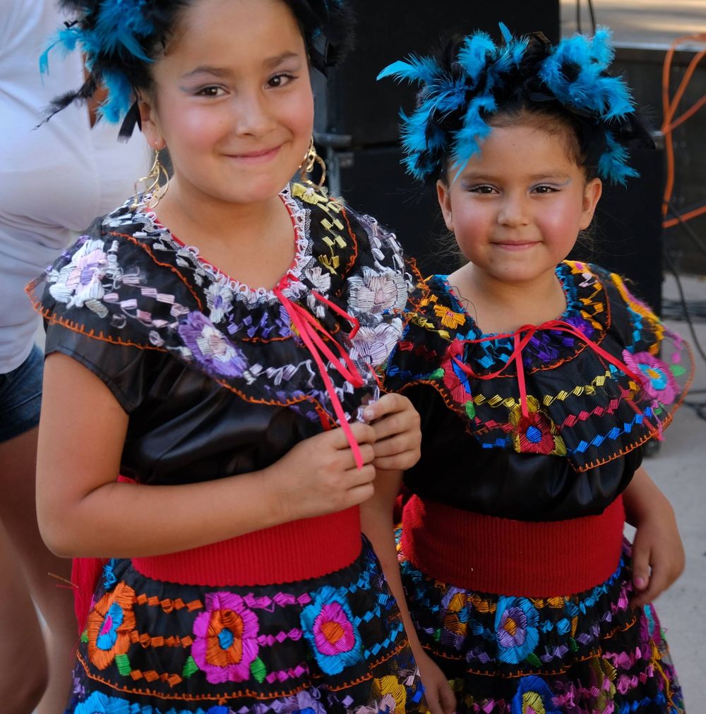 Young dancers in colorful Mexican folk dresses with bright feather accessories and embroidered details perform at a festival.  Santa Fe, NM.