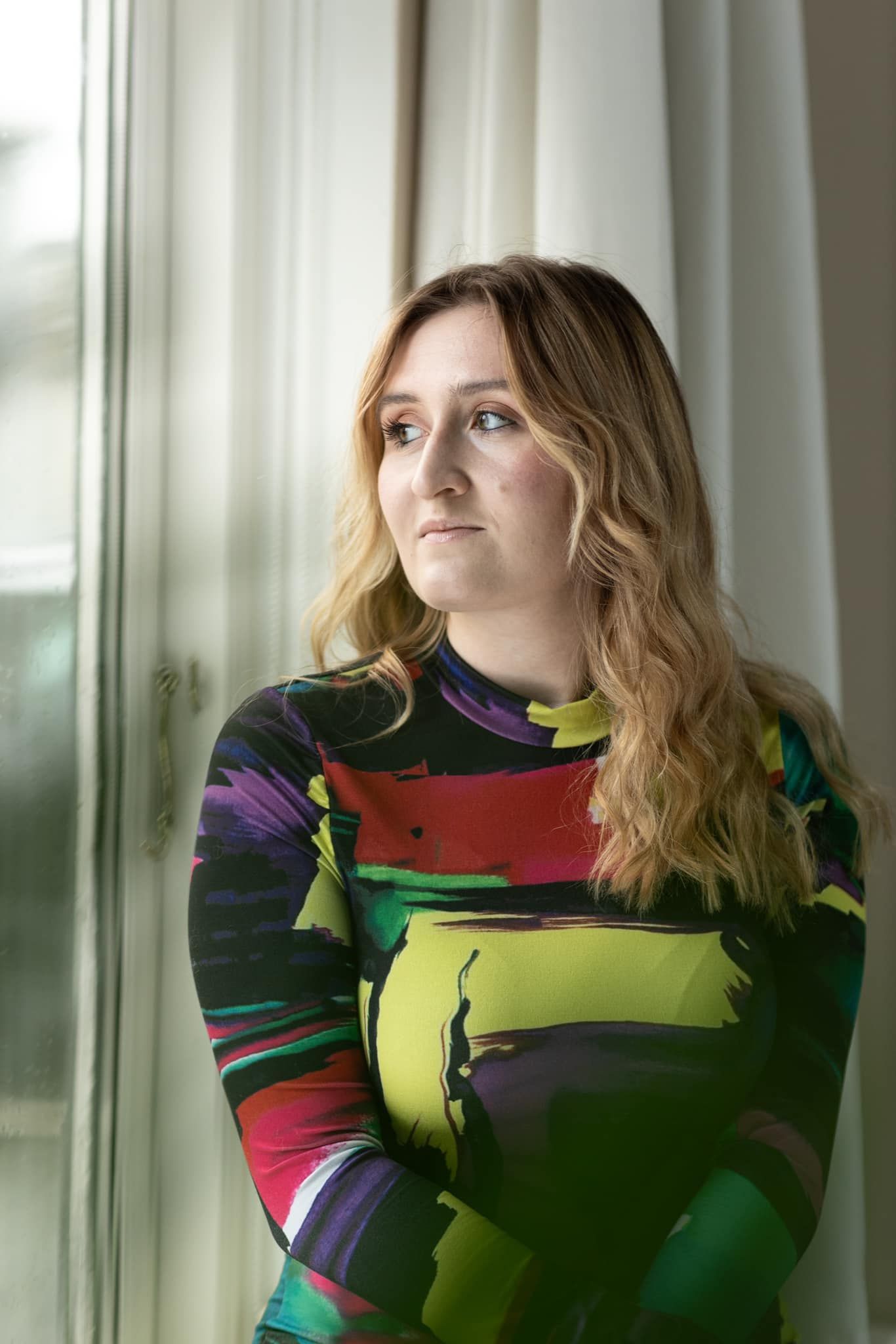 Person wearing colorful striped sweater poses near window in natural lighting.
