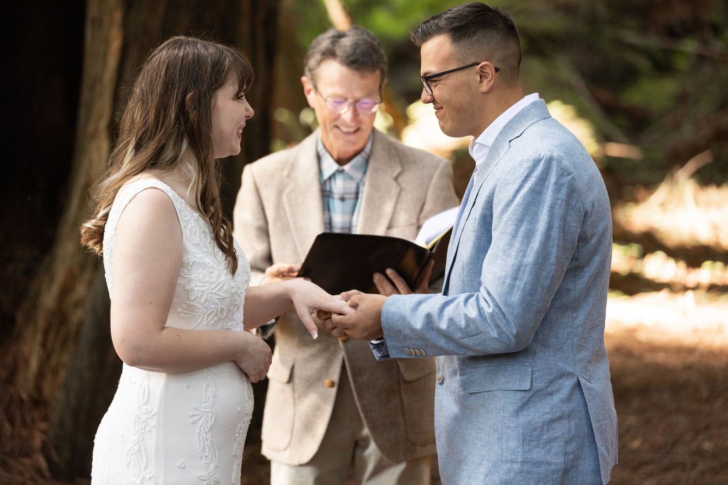 Couple exchanging vows with officiant during intimate outdoor wedding ceremony in redwood forest.