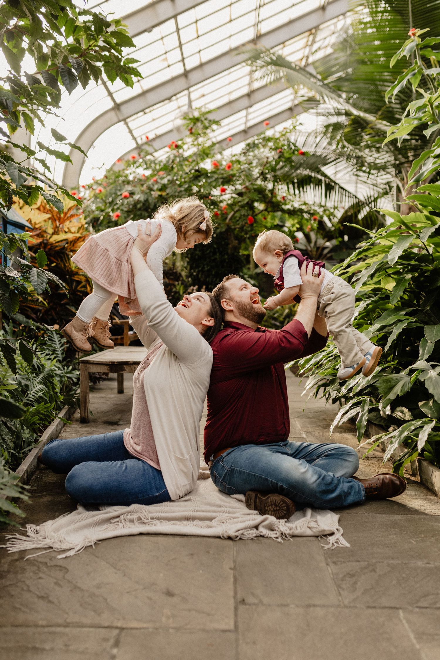A couple lounging in a greenhouse surrounded by lush plants and natural light.