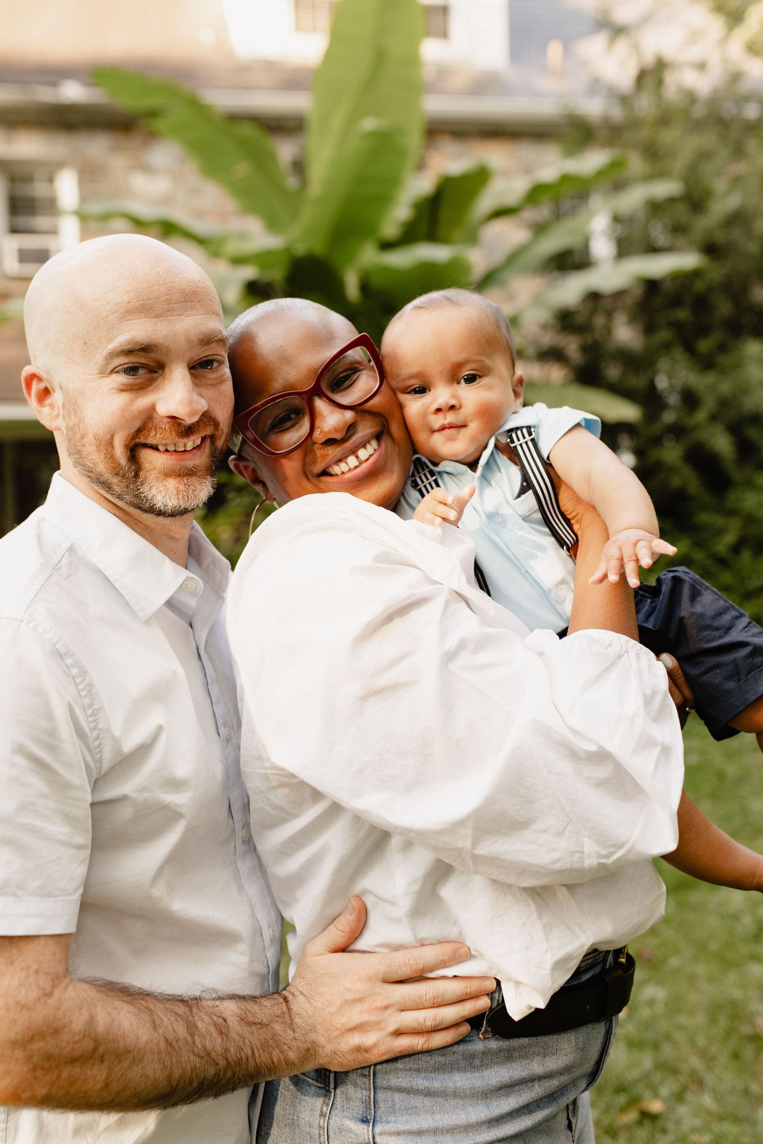 Family shares joyful embrace in sunny garden setting.