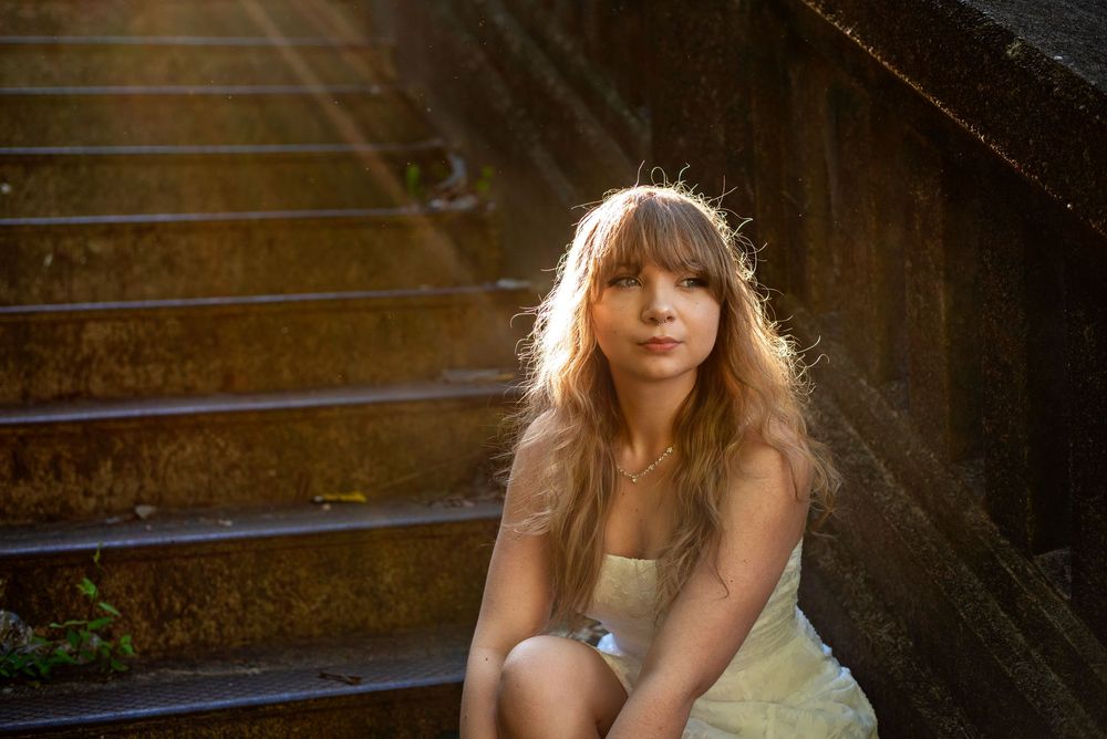 A backlit figure sits on outdoor stone steps during golden hour with sunlight creating a warm atmospheric glow.