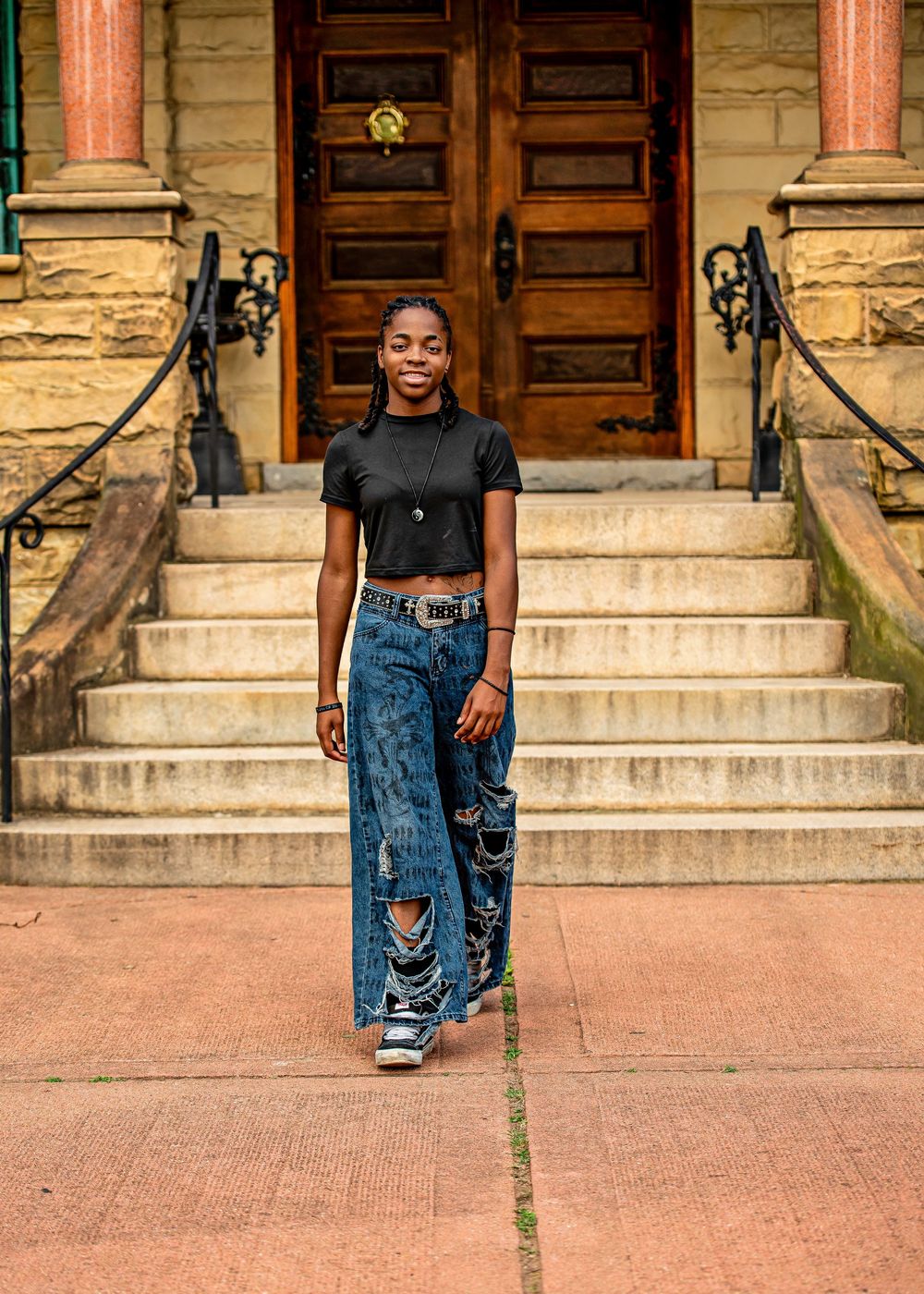 Young woman in ripped jeans and black crop top poses confidently on stone steps of historic building.