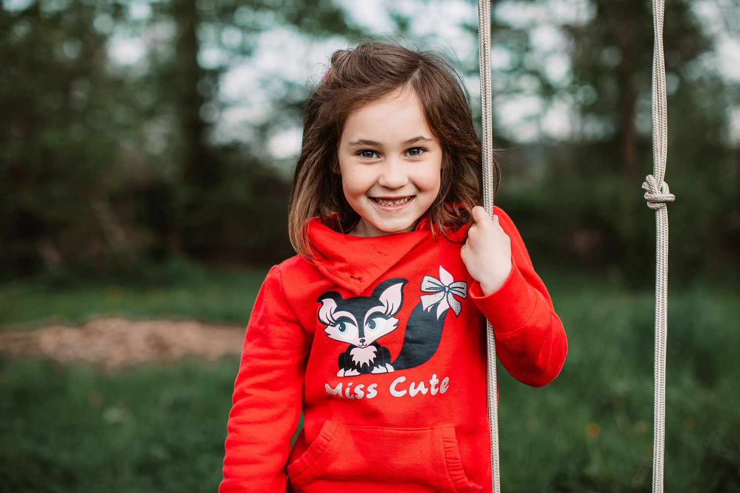 A child wearing a red fox sweater smiles joyfully while playing outside.