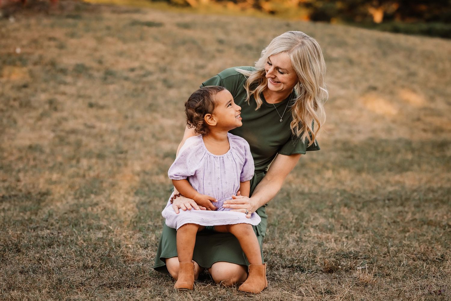 A heartwarming outdoor moment shared between parent and child sitting together in a grassy field at sunset.