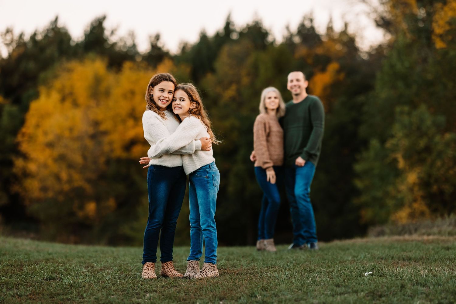 Family portrait outdoors with fall foliage and green sweater coordination.
