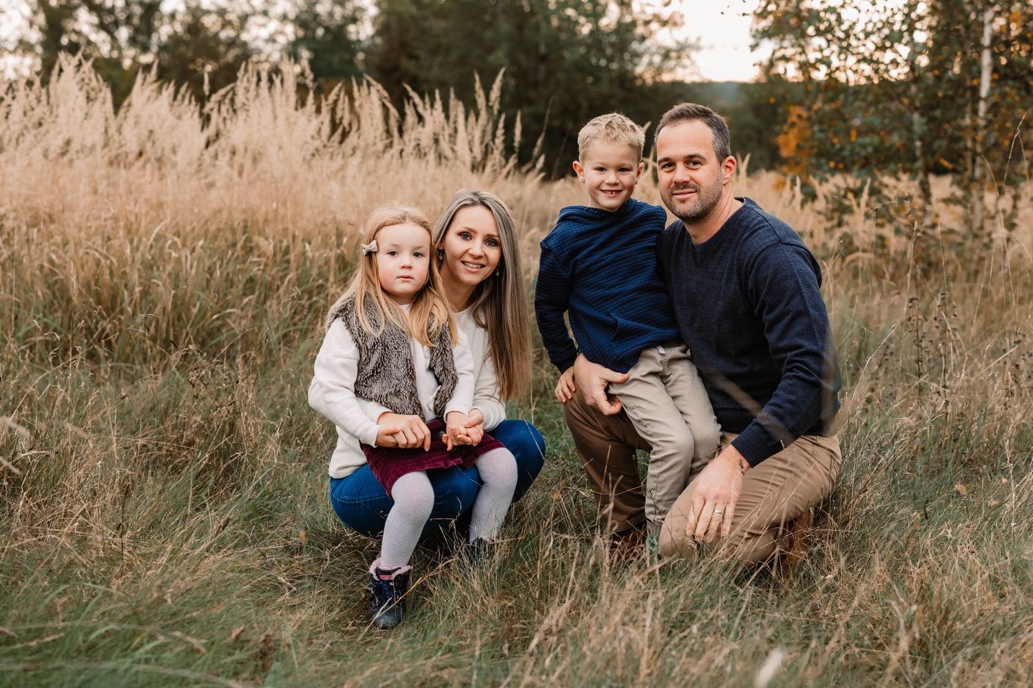 Family poses together in tall grass during sunset photoshoot.