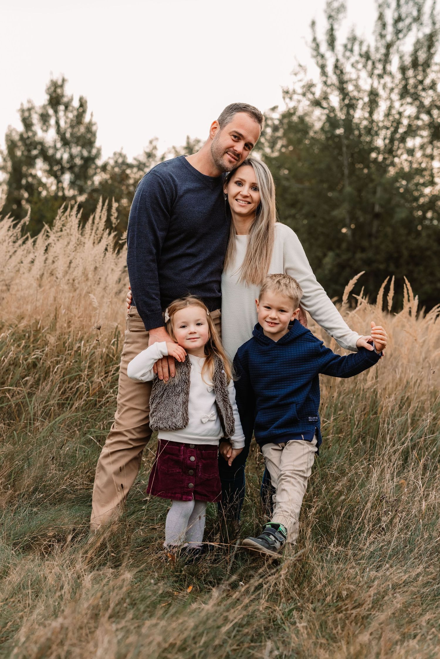 Candid family portrait in tall autumn grass field with warm sunset light and natural outdoor setting.
