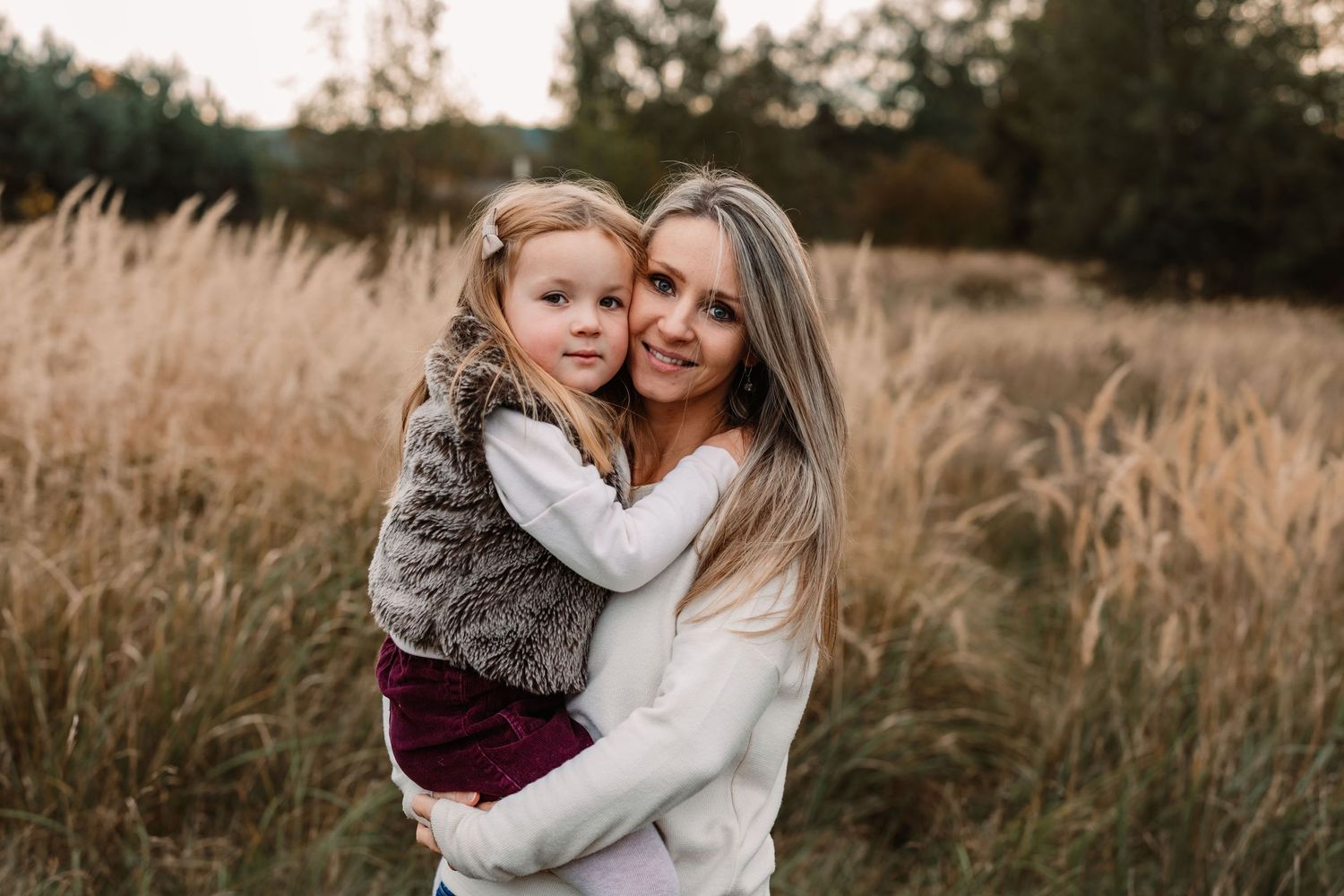Mother and child share warm embrace in field of tall grass at sunset.