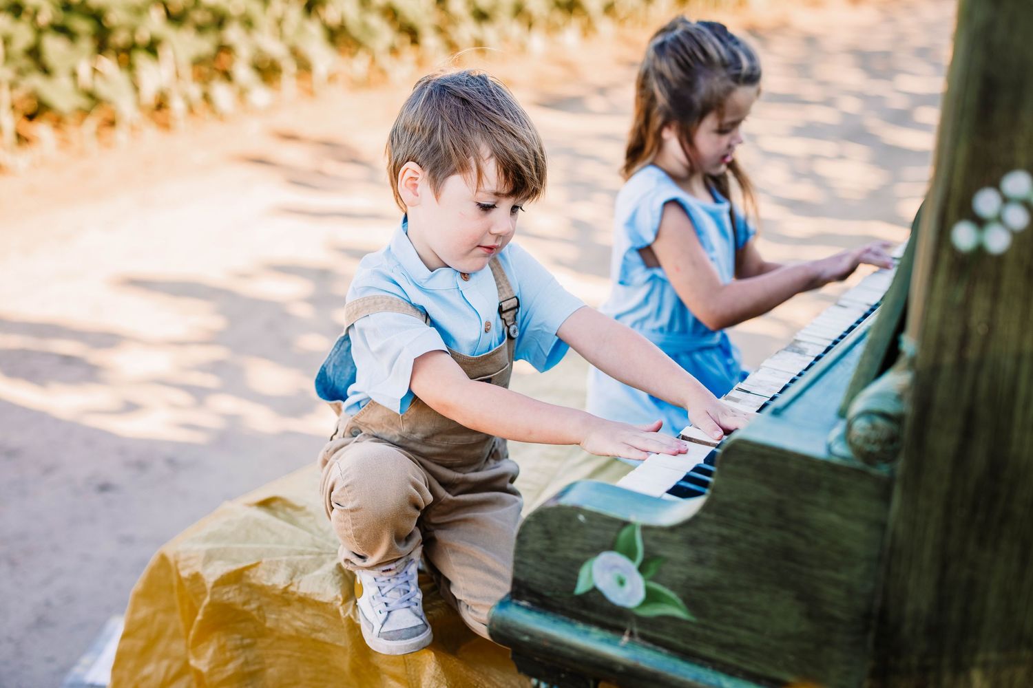 Two children playing a vintage outdoor piano together on a sunny day.