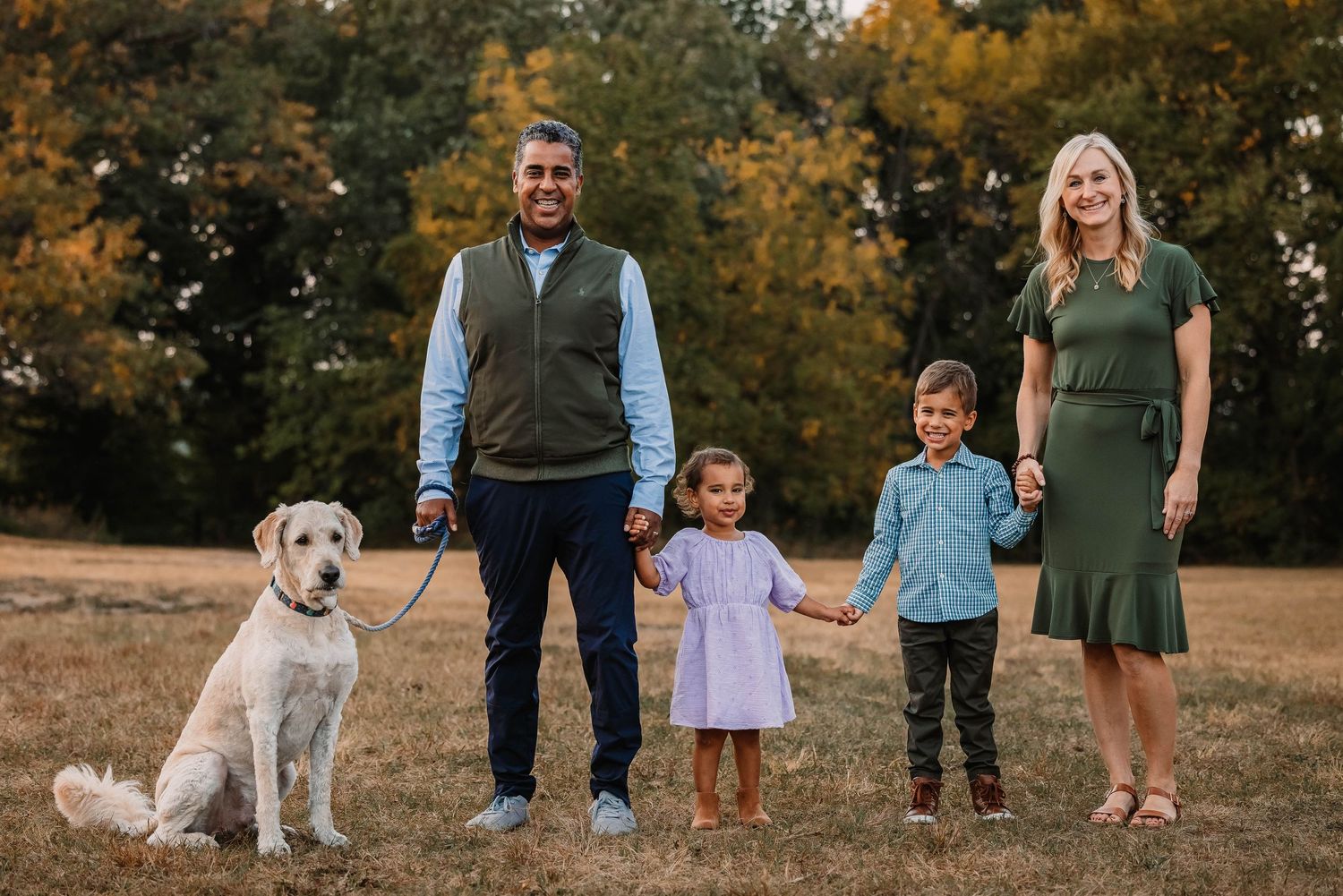 Family portrait with dog in autumn setting with golden trees.