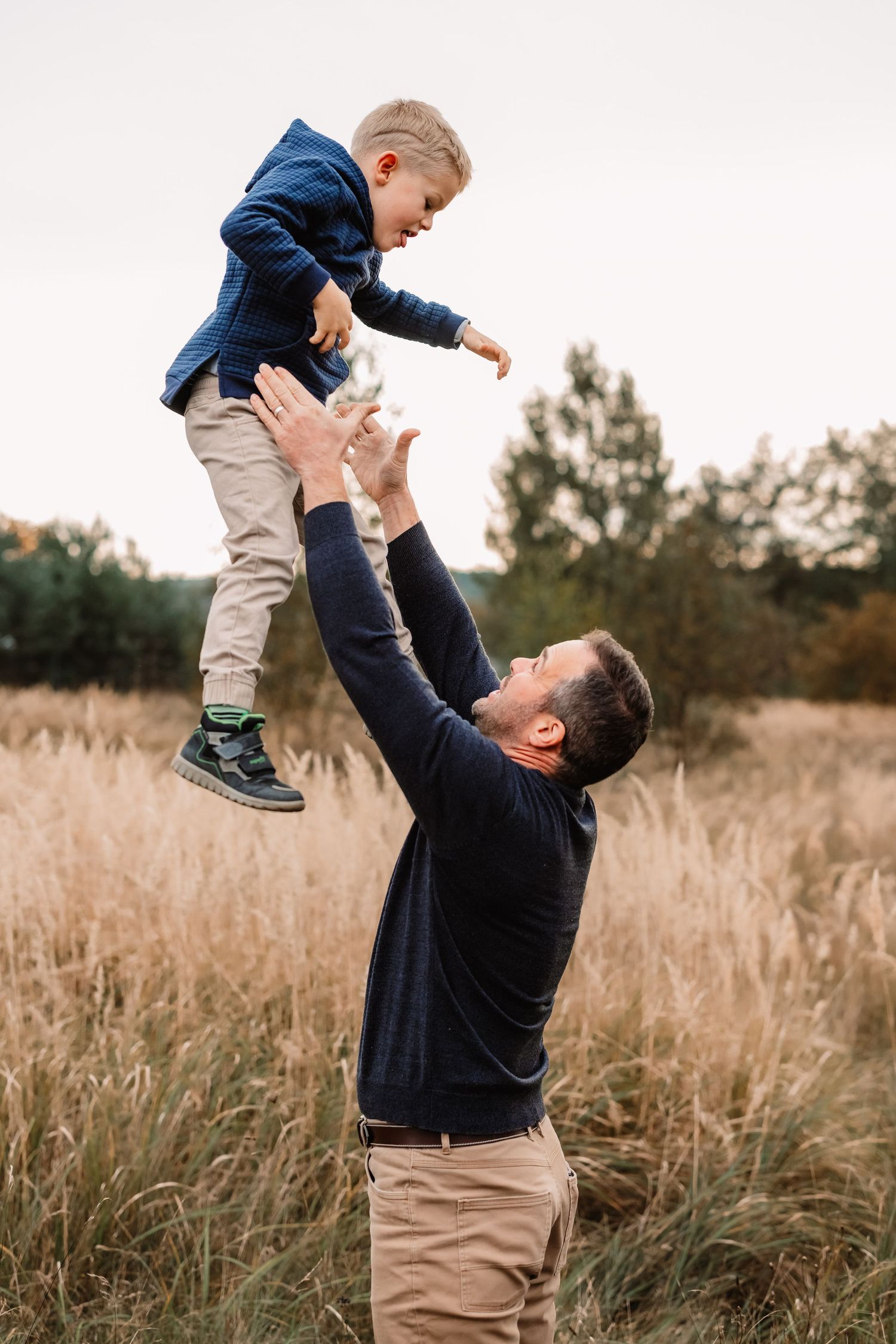 Parent lifts child high in the air while playing in autumn field.
