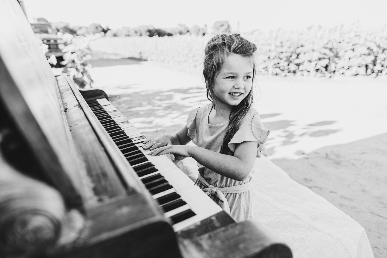 Black and white vintage photo of a child playing piano outdoors.