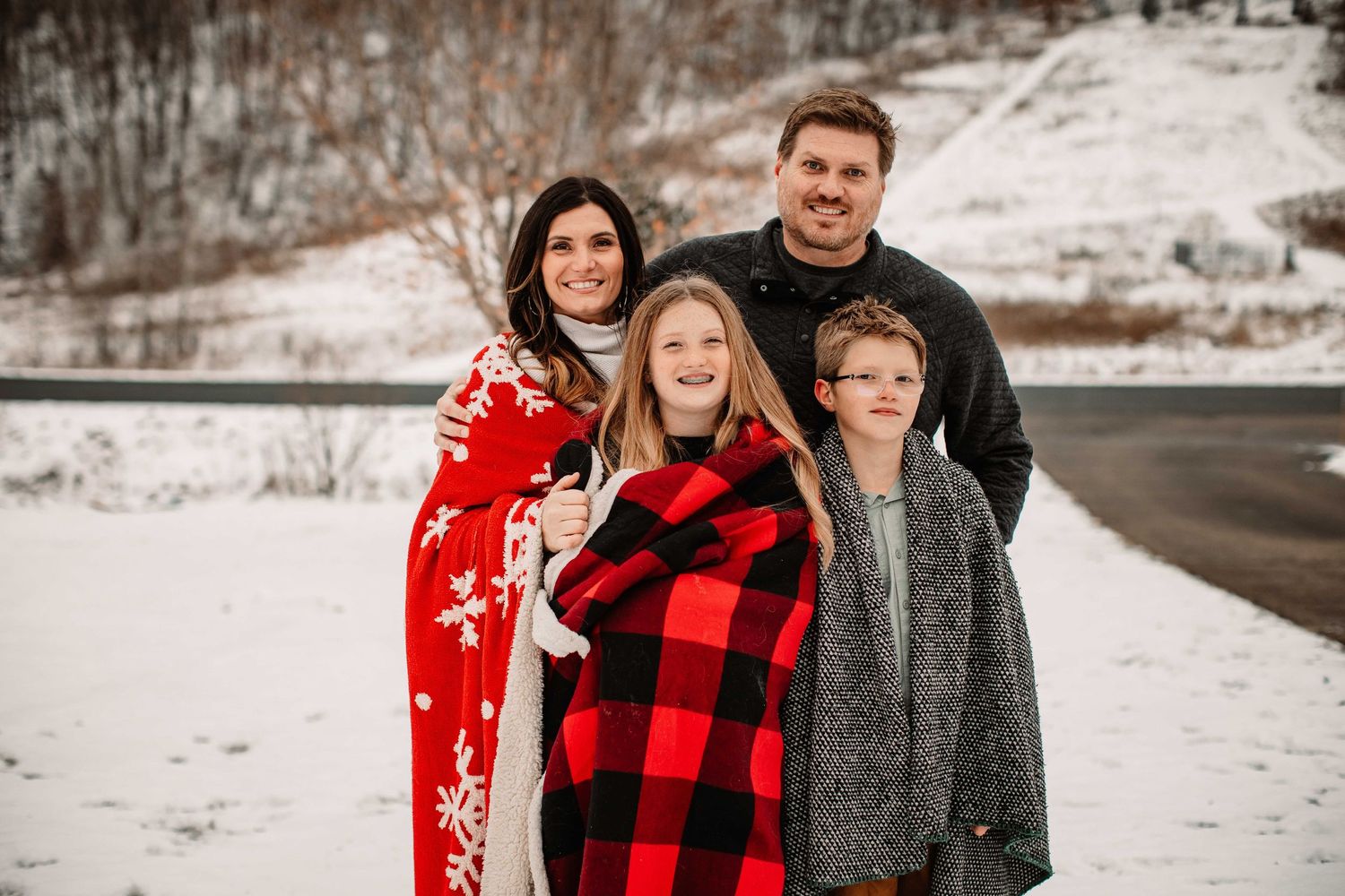 A family wrapped in cozy blankets poses together in a snowy winter landscape.