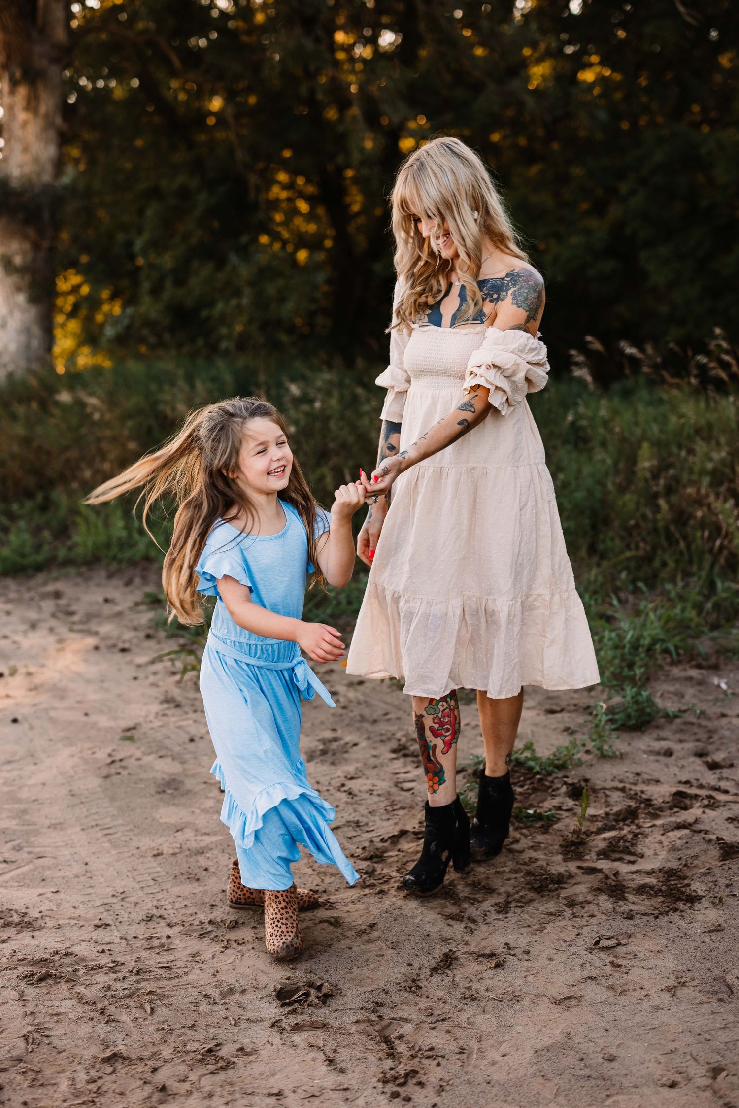 A parent and child holding hands and dancing together on a dirt path surrounded by trees.