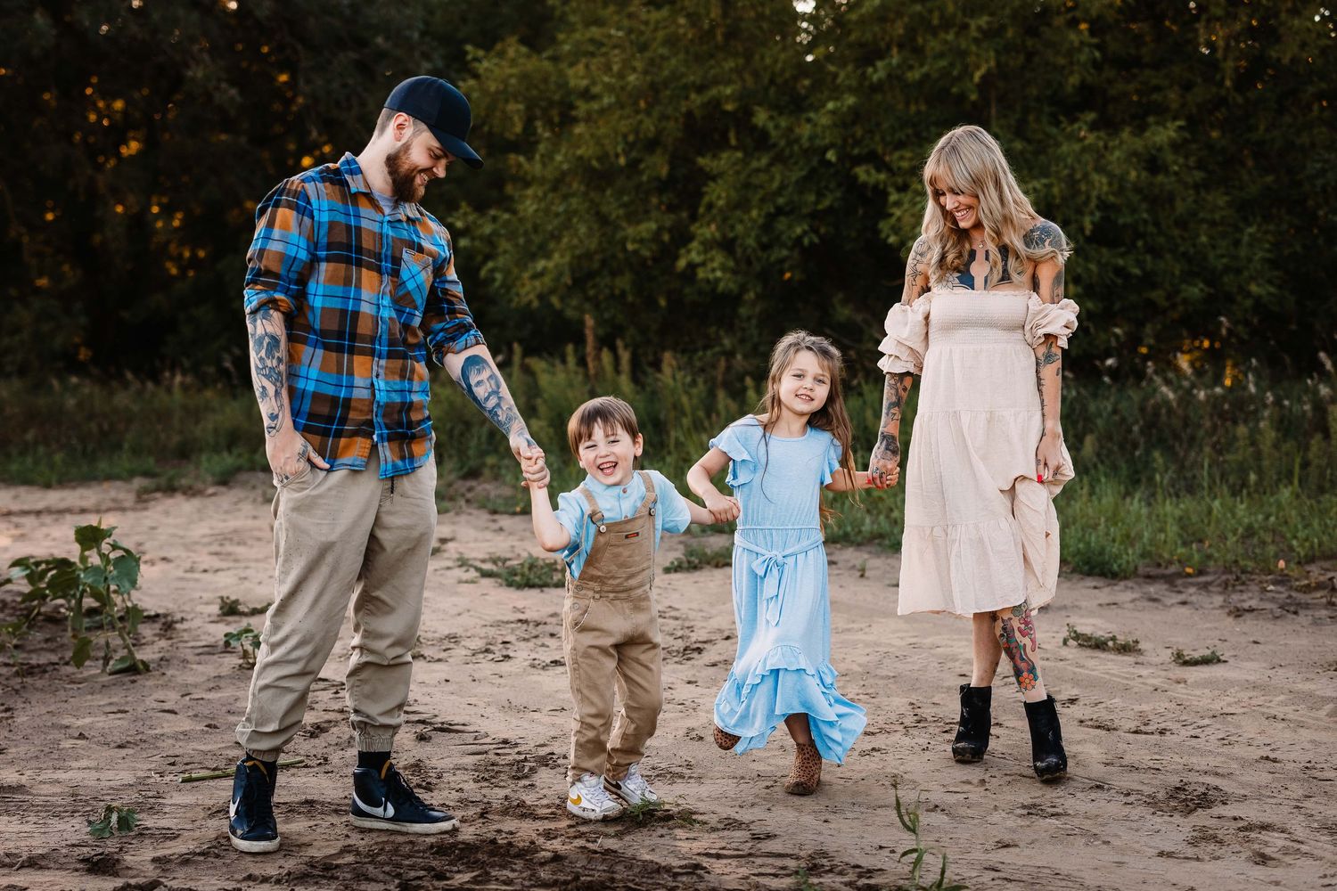 A family of four walking hand in hand on a dirt path through nature at sunset.