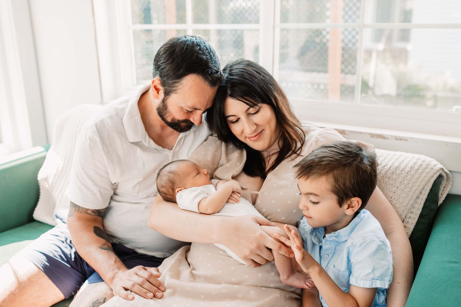 Happy family with two young children sitting together on couch and sharing tender moments at home.