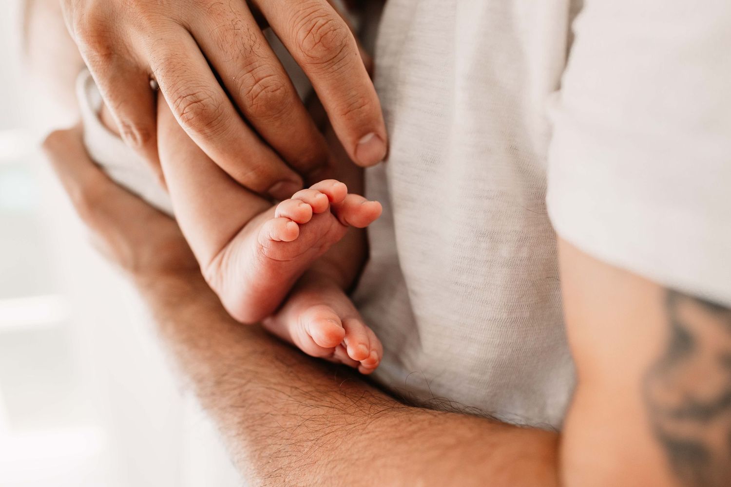 Close up view of person's hands holding newborn baby's feet with soft natural lighting.