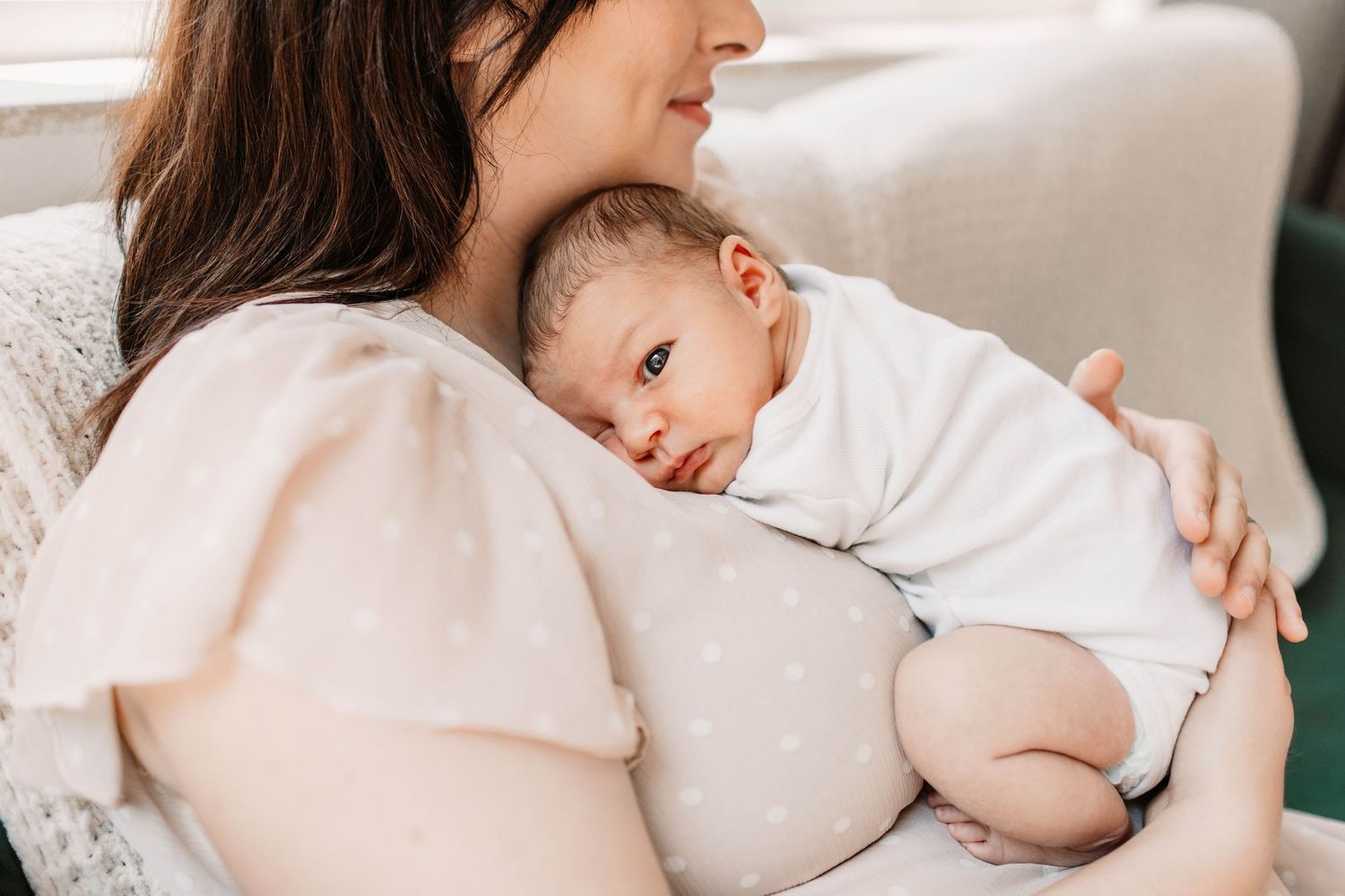 A mother and baby wearing white clothing cuddle together sweetly during an intimate photo session.