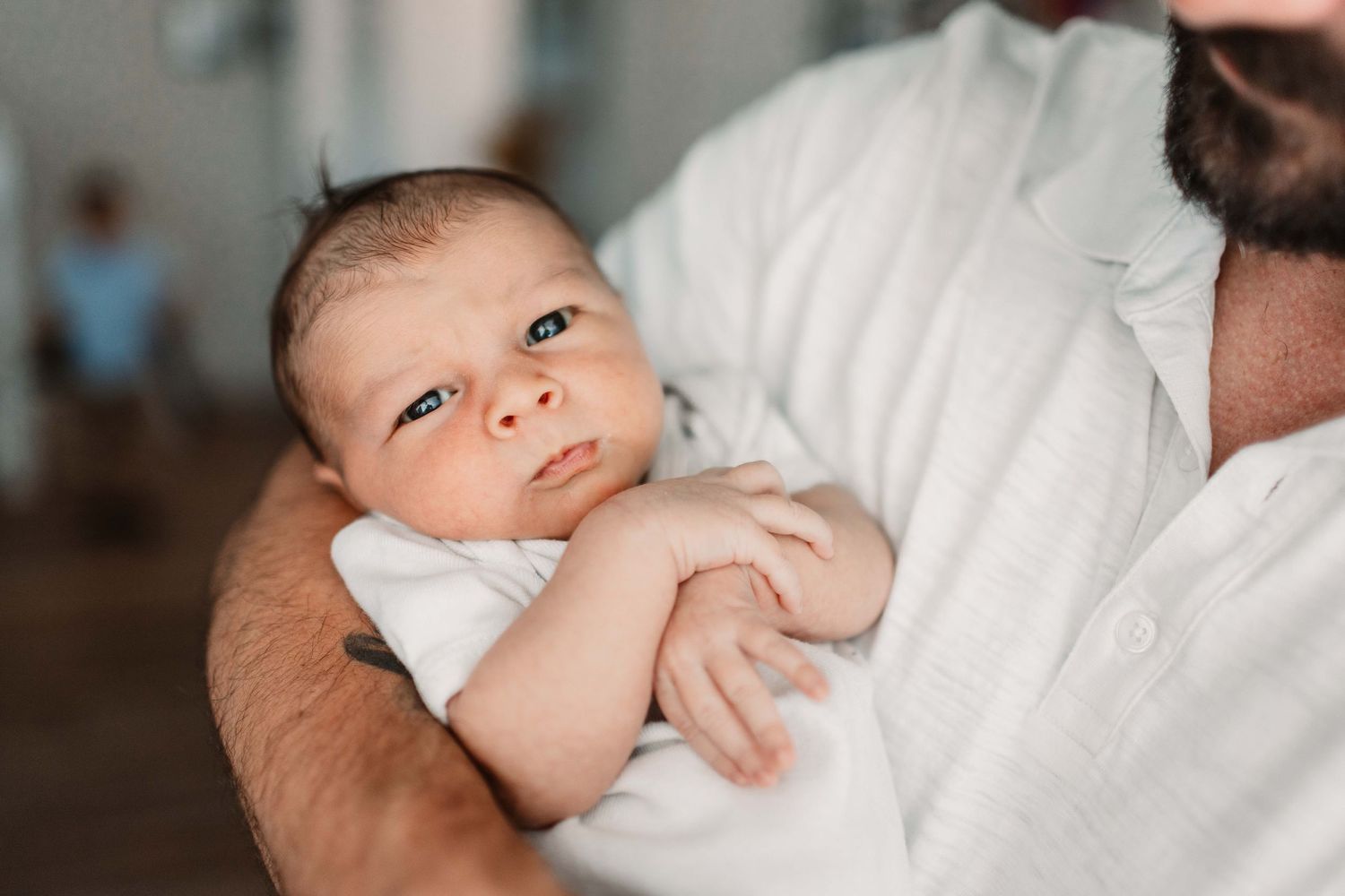 A series of photos showing an infant being held in white blankets against soft, warm lighting.