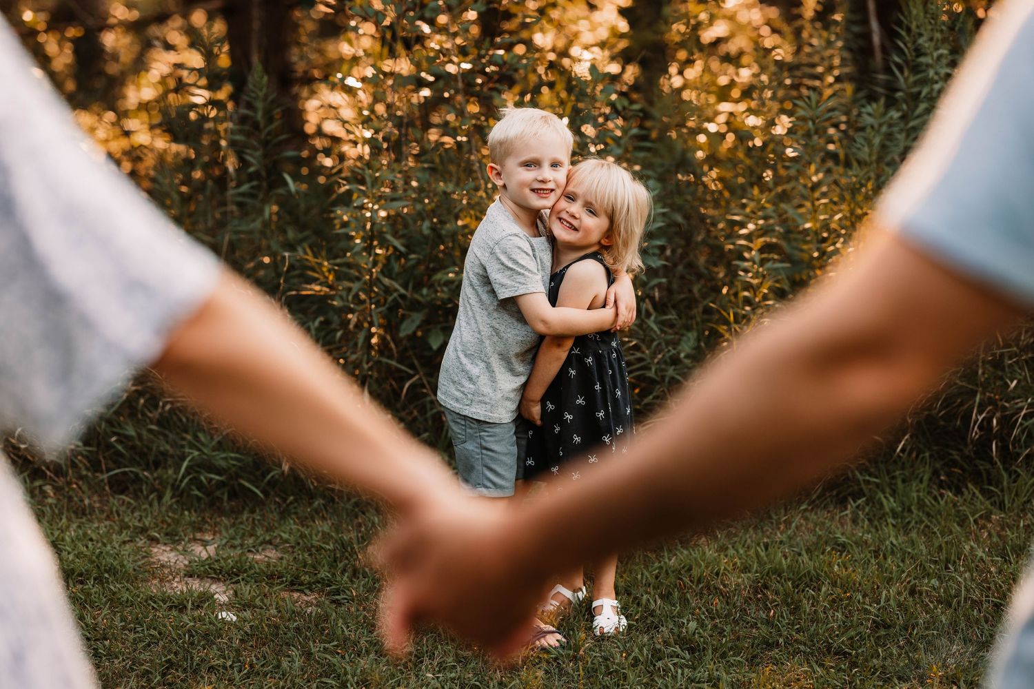 Sunset photo in garden with silhouetted hands in foreground framing children.