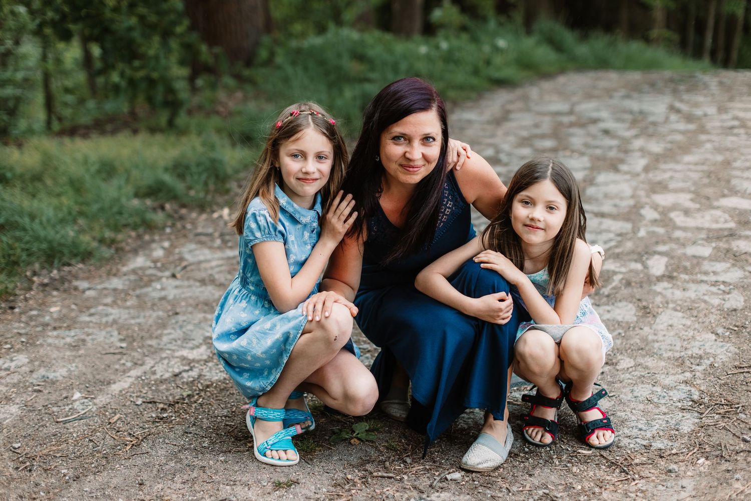 Three people crouch together on a wooded path during an outdoor photography session.