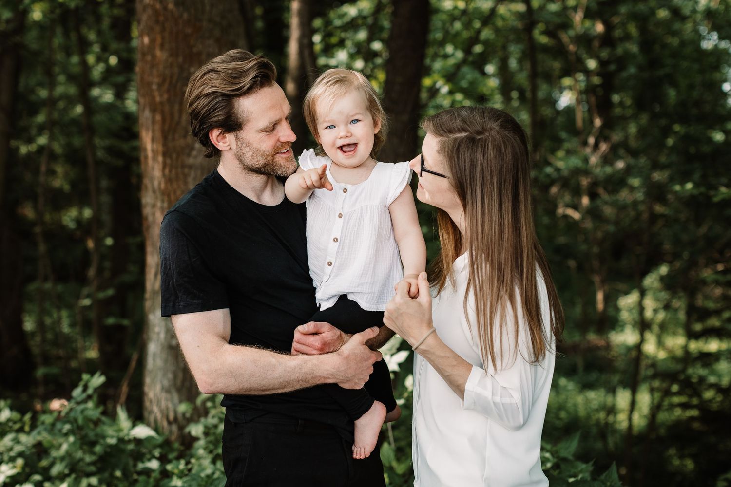 A sweet family moment captured in a sunlit forest setting.