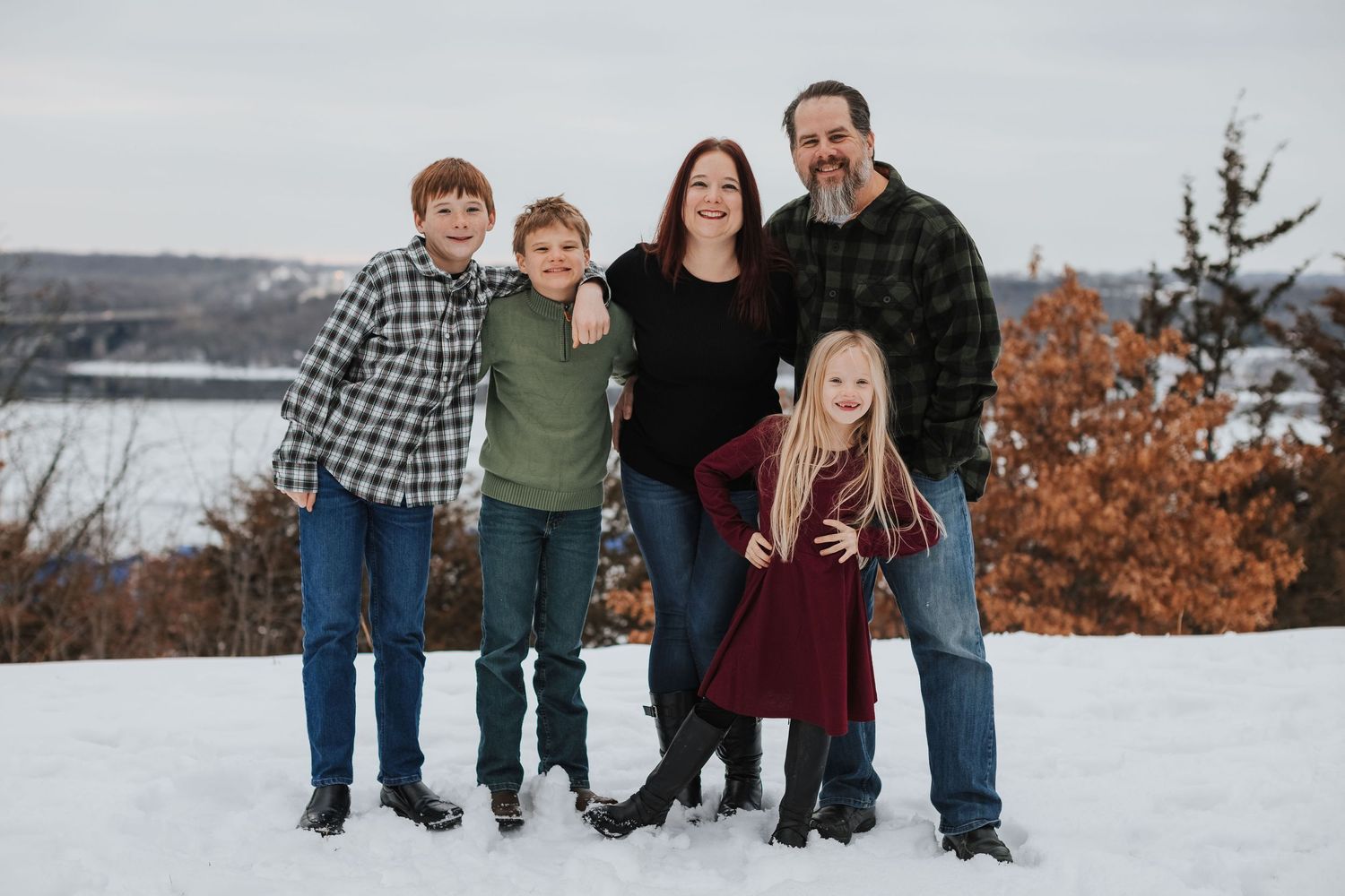 A family of five poses together for a winter portrait with a lake and autumn trees in the background.