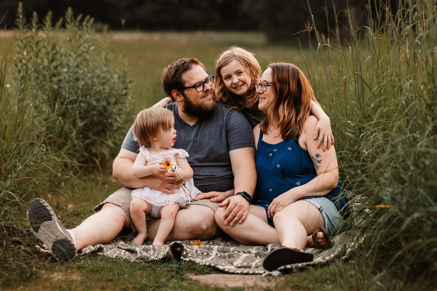 Family sharing intimate moment while sitting together on blanket in tall grass.