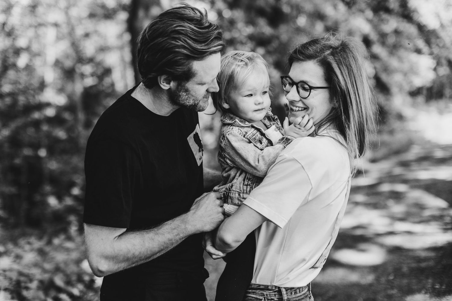 Black and white portrait of family sharing intimate moment on wooded path.