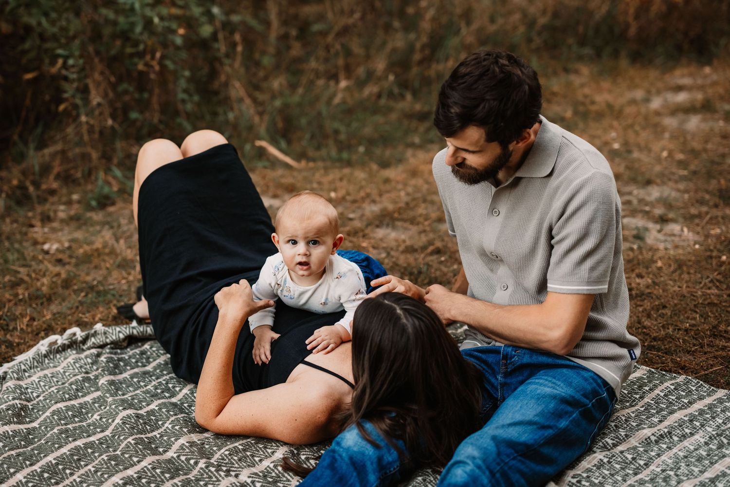 Family relaxing together on a blanket outdoors during a golden autumn afternoon.
