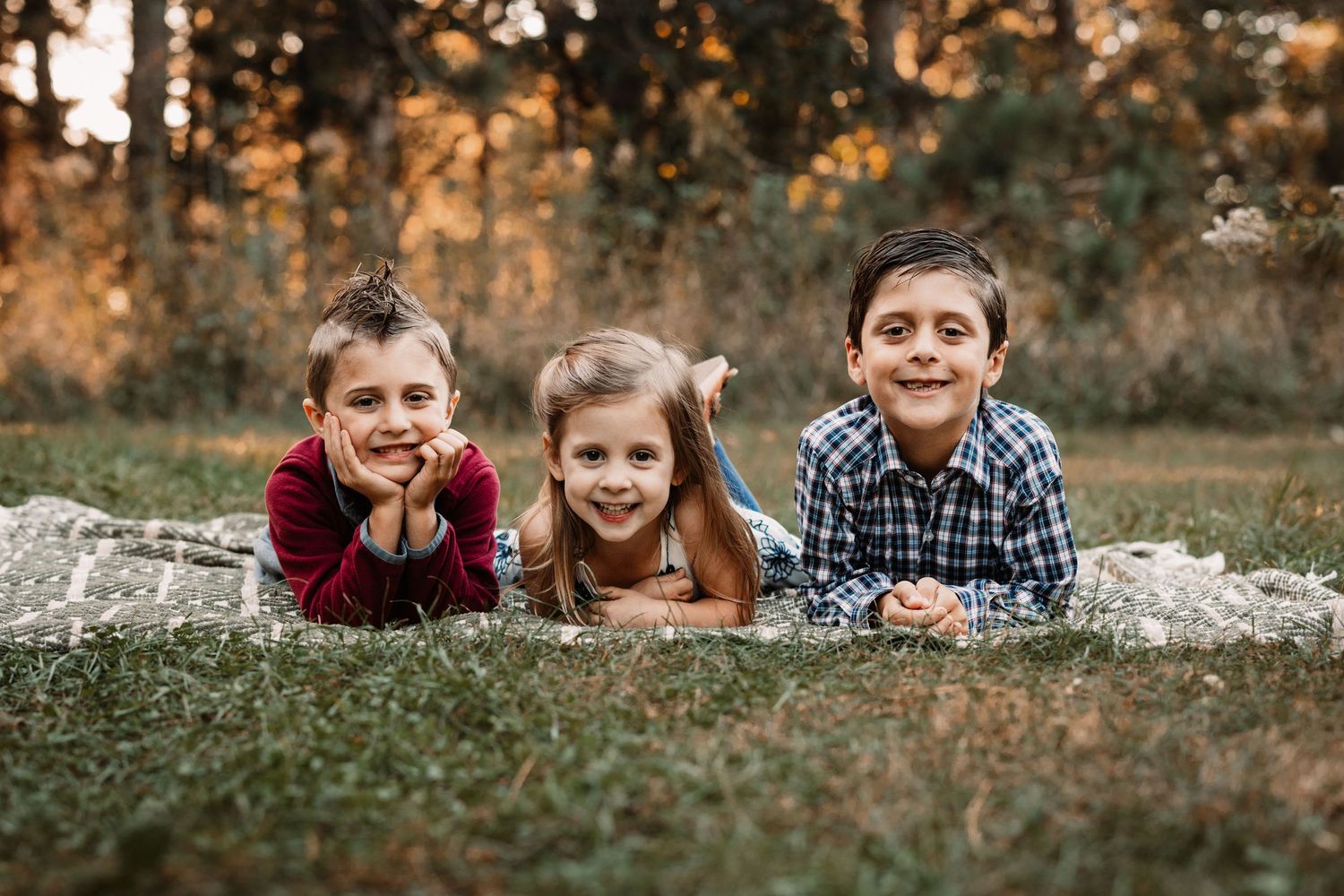 Three children lying on ground smiling during autumn sunset photo session.