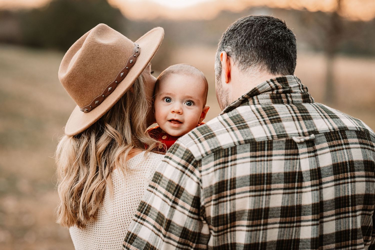 Intimate family embrace outdoors with person wearing brown hat and plaid shirt against autumn backdrop.