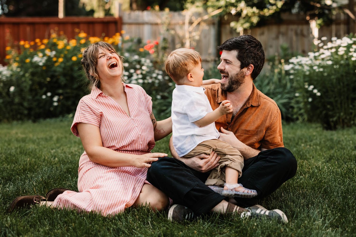 Family sitting together on grass enjoying tender moments in a park during golden hour sunset light.