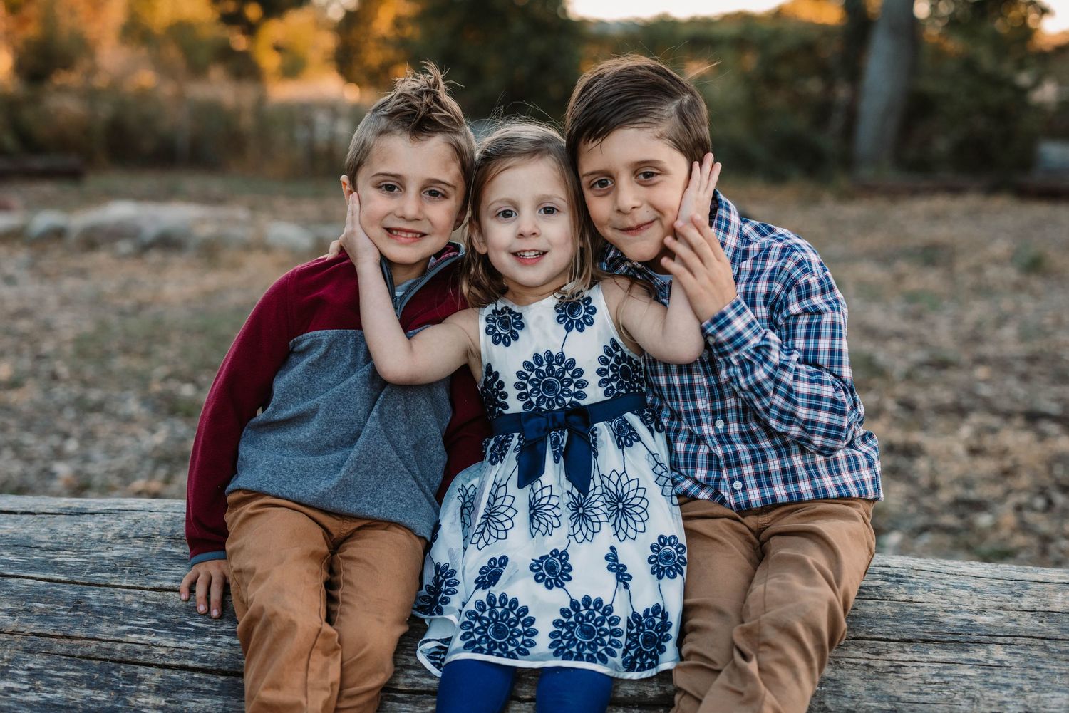 Three siblings sitting together outdoors during golden hour photography session.