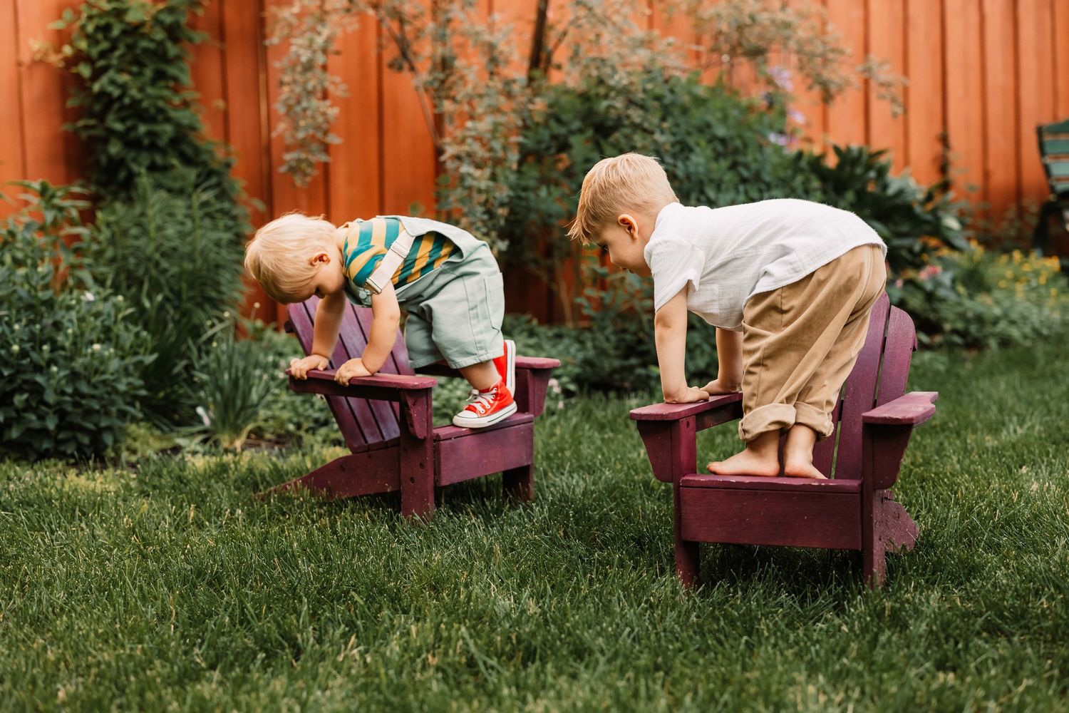 A series of red adirondack chairs positioned in a grassy area against an orange painted wall.