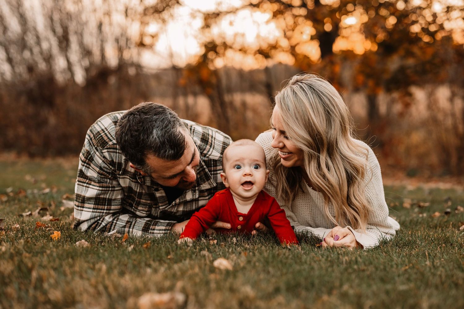 Sweet family moment laying on grass during golden hour in autumn setting.