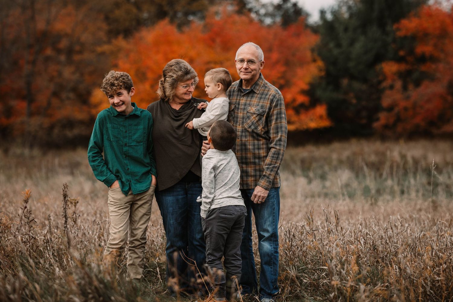 A family stands together in a field with vibrant orange fall foliage in the background.