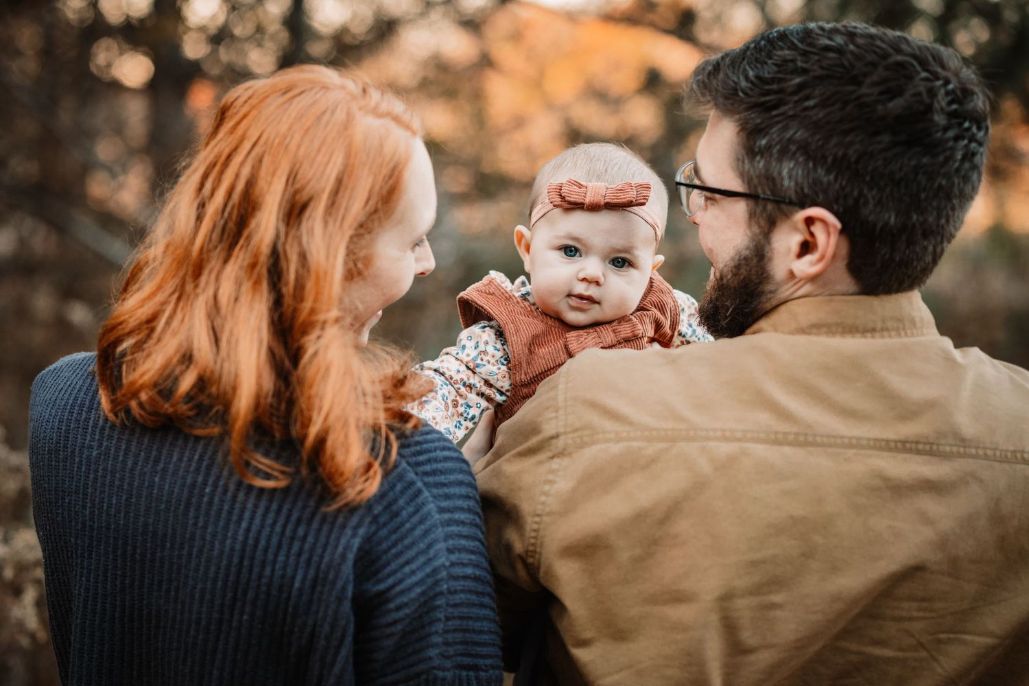 Couple spends tender moment with baby outdoors during golden hour.