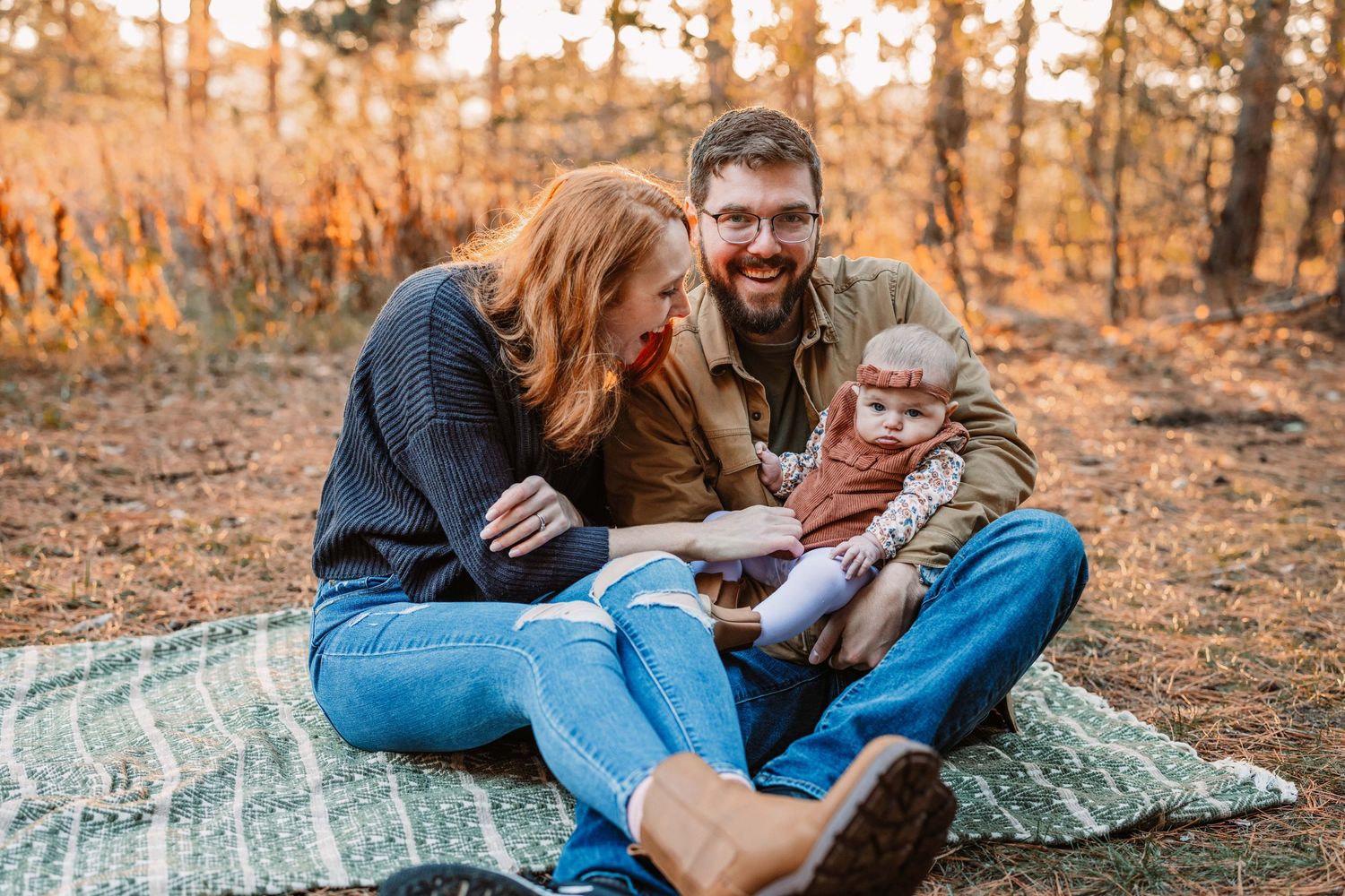 Family relaxes together on picnic blanket in autumn forest setting.