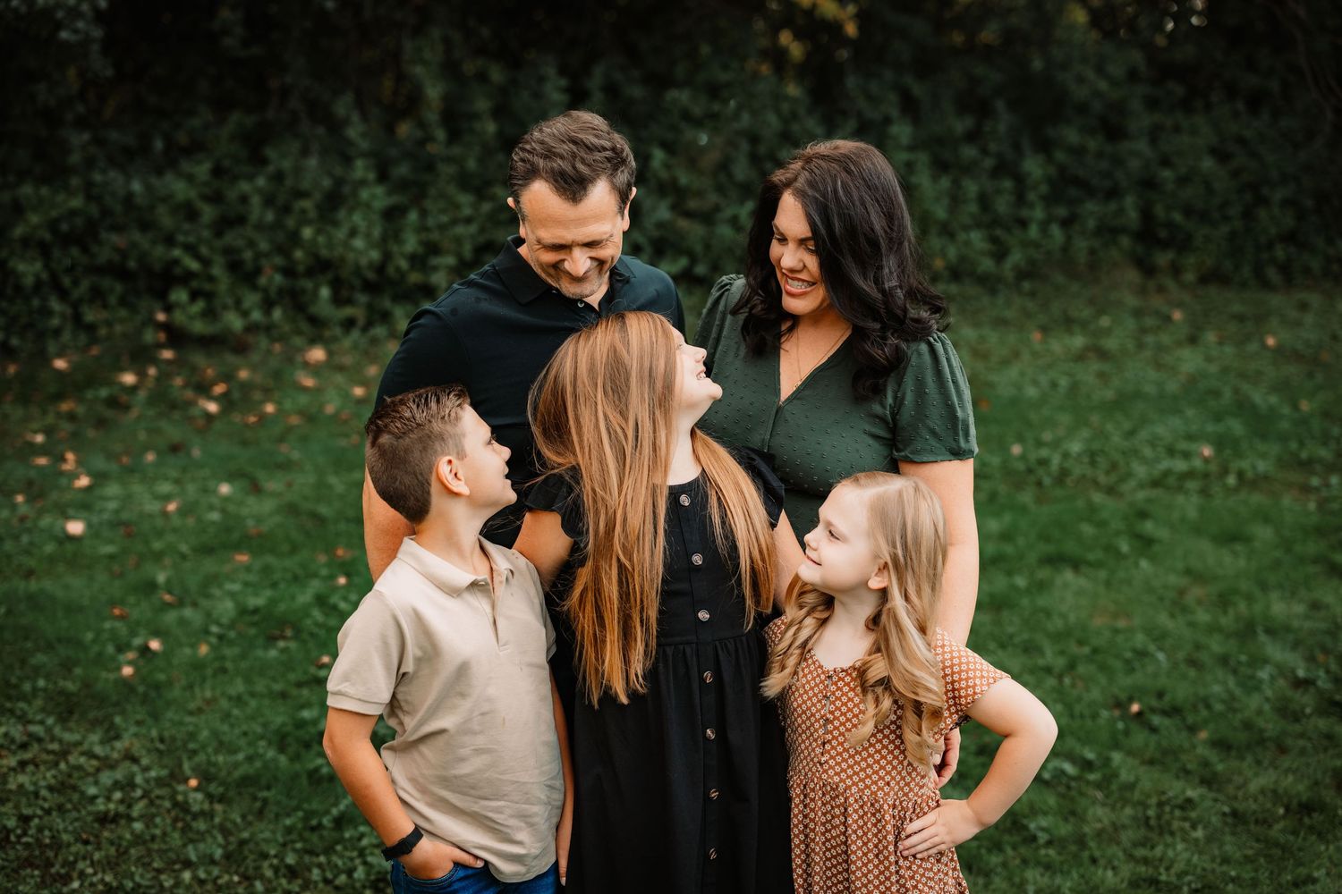 Family of five sharing joyful moment together in backyard garden setting.