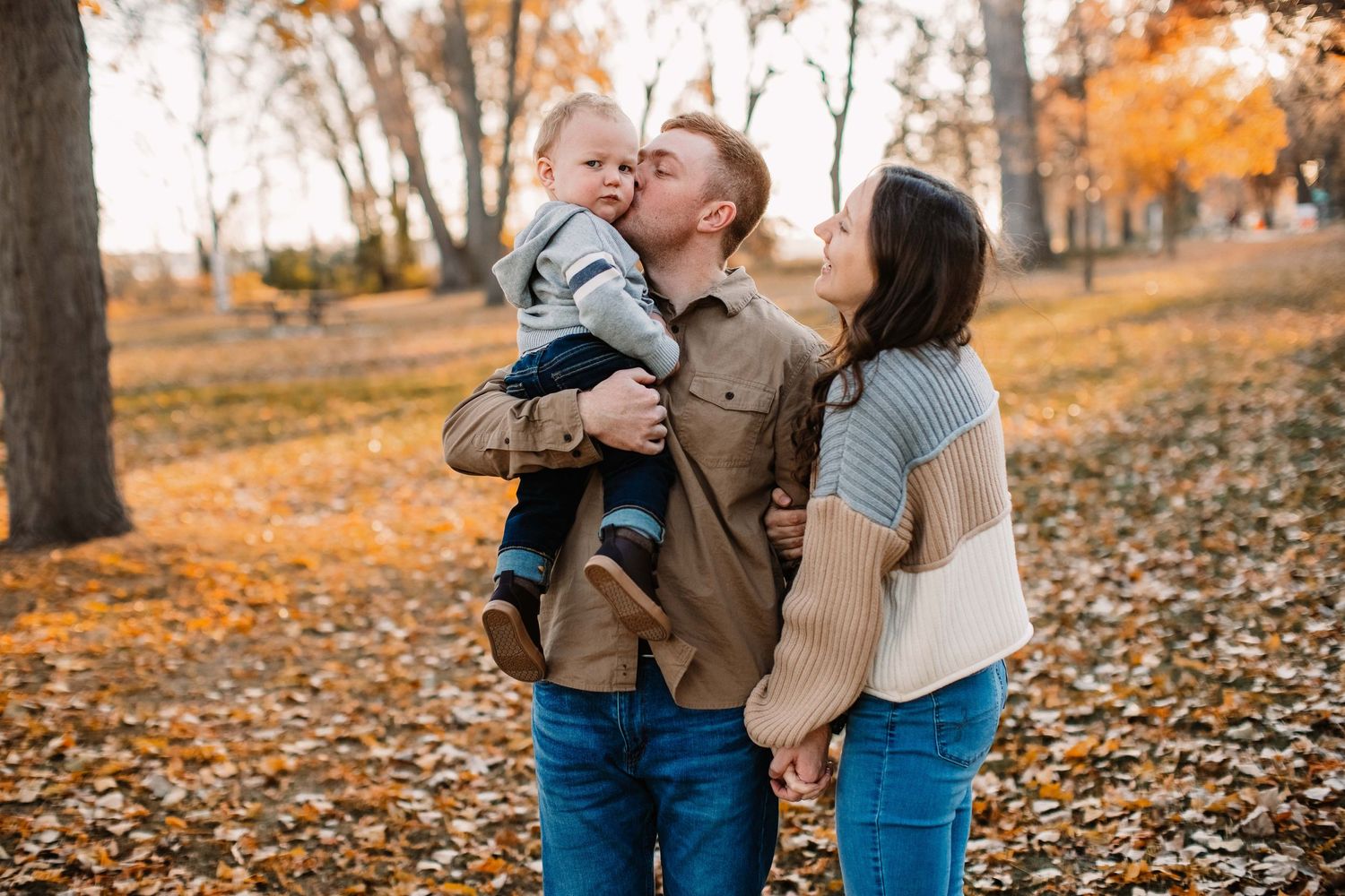 A sweet family moment shared among fallen autumn leaves in a park.