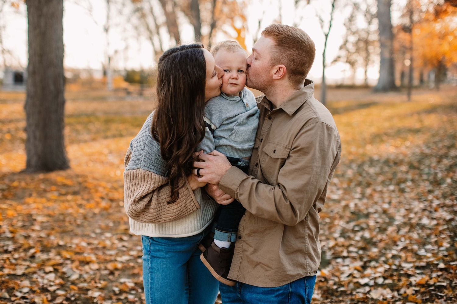 A tender family moment captured in an autumn setting with fallen leaves.