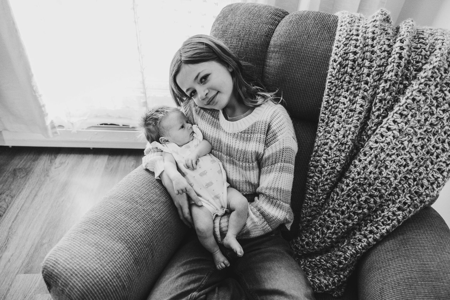 A nurturing scene of an adult and infant resting together on patterned fabric in warm lighting.