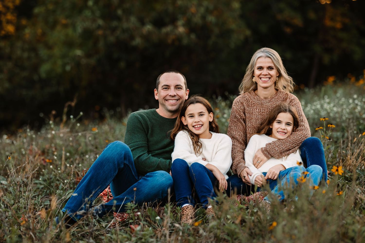 A smiling family of four sitting together in a wildflower meadow during golden hour.