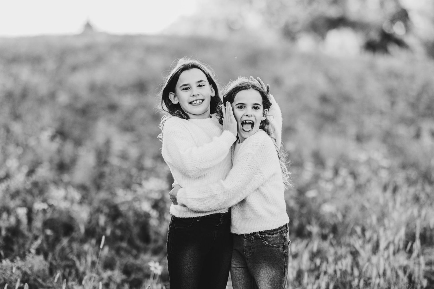 Black and white photo of two people embracing and laughing together in a grassy field.