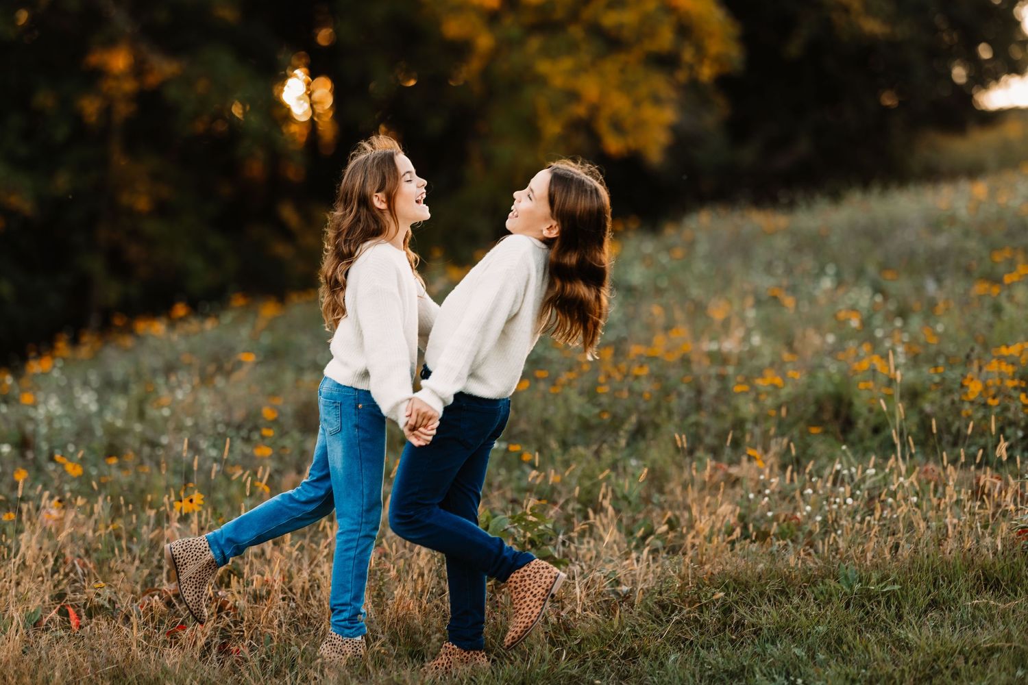 Two people in matching outfits dancing and laughing together in a golden field at sunset.