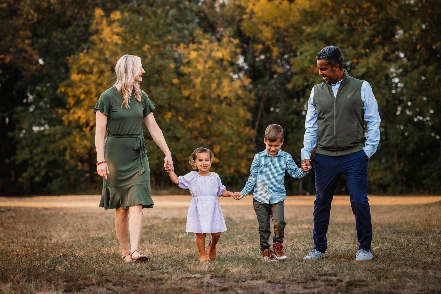A family of four takes an evening stroll together on a path with golden autumn trees in the background.