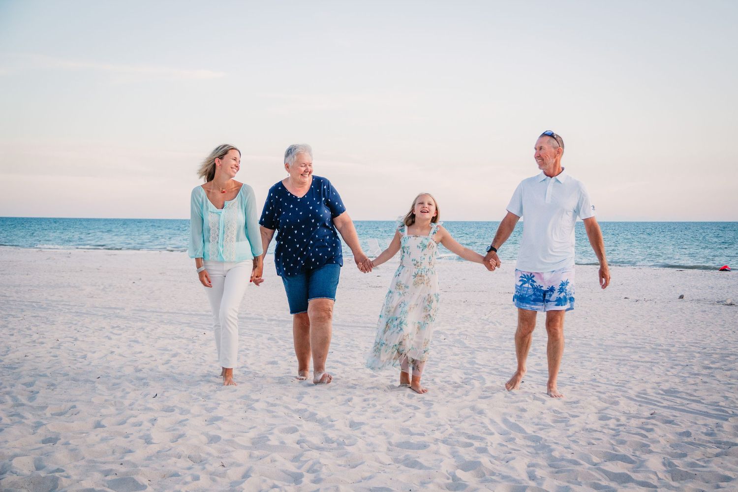 A family holds hands while walking together on a white sandy beach at sunset with the ocean in the background.