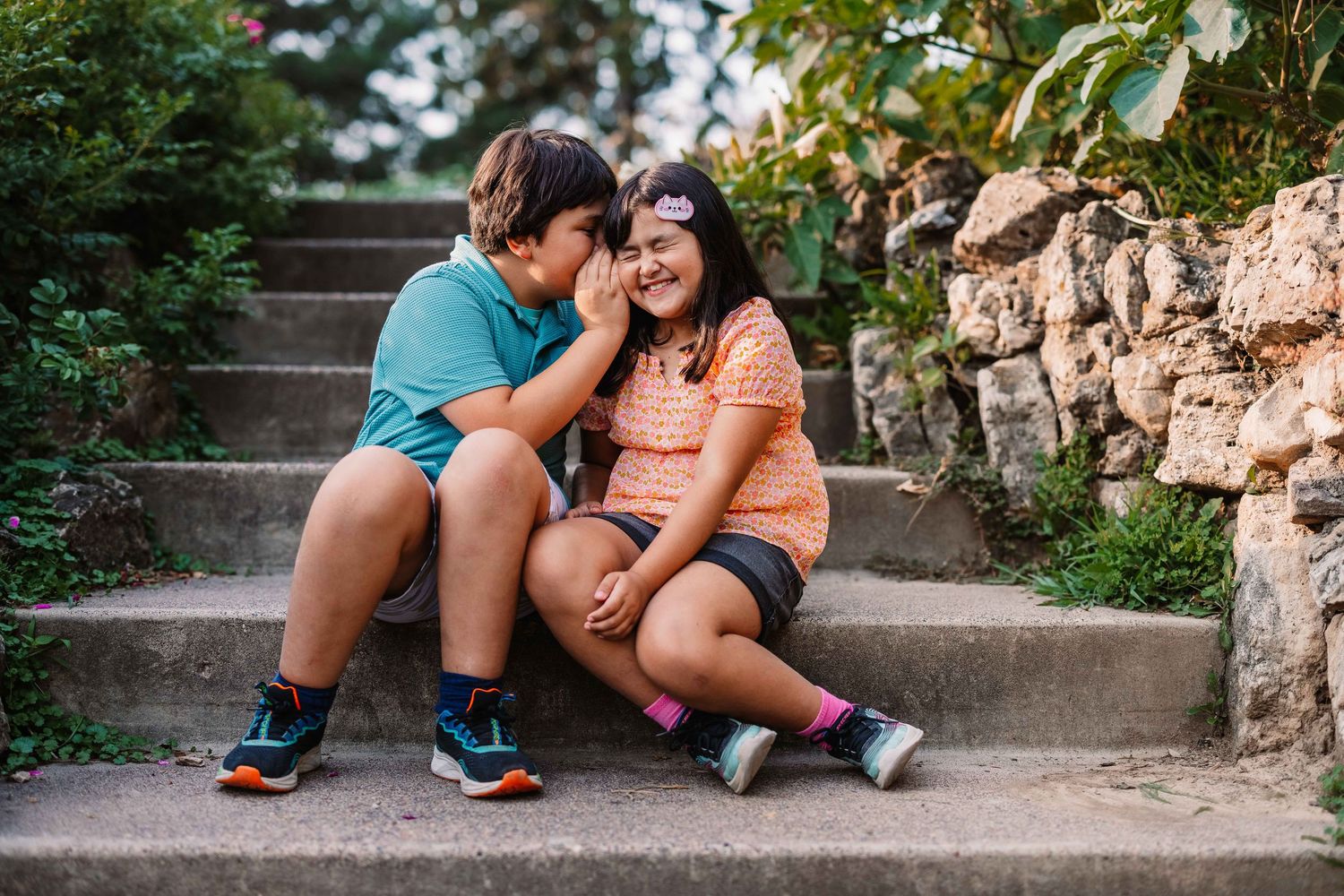 Two people sitting close together on concrete steps in an outdoor setting wearing casual clothing and sneakers.